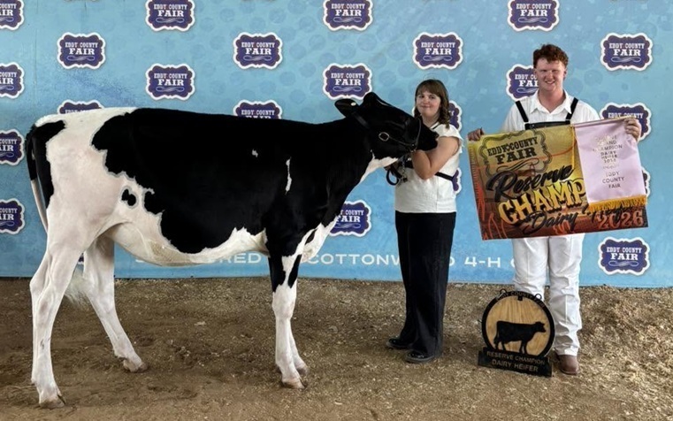 A teen girl stands next to a black-and-white cow while a teen boy holds a banner beside her.