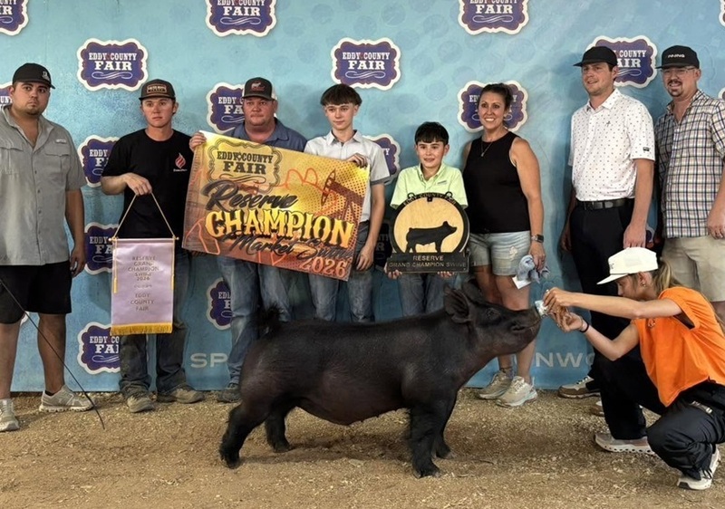 A teen boy stands behind a black pig with several people alongside him, three of whom are holding banners.