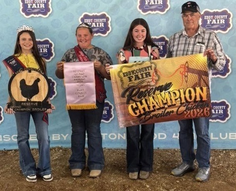 A teen girl and a man hold a banner alongside two other teen girls, also holding banners.