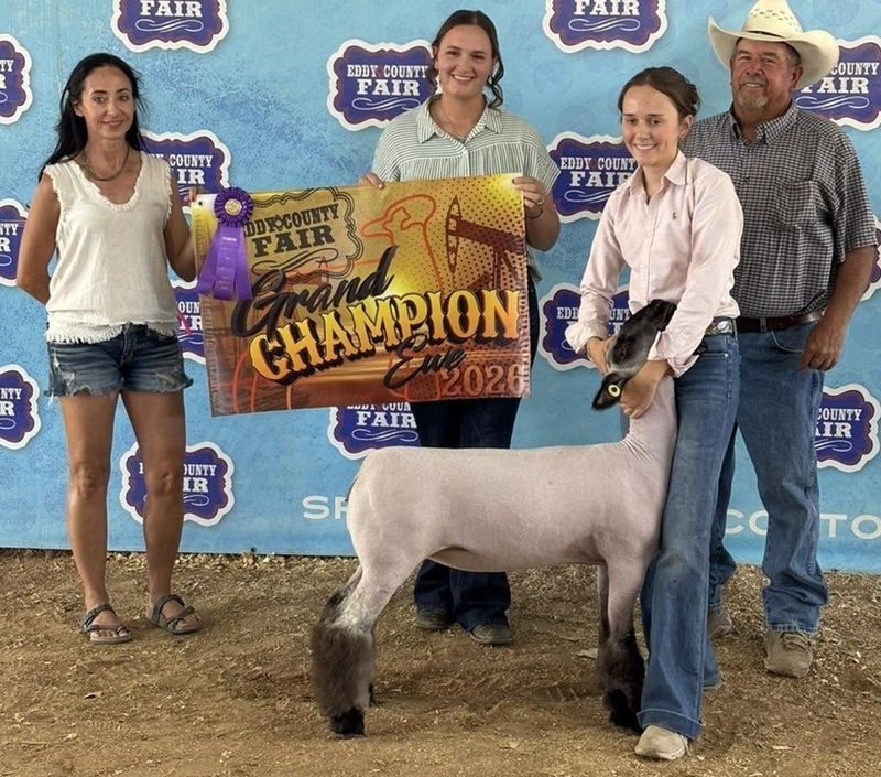 A teen girl holds the head of a shaved black-and-white sheep. Two females stand behind her holding a banner and one male stands to the side.