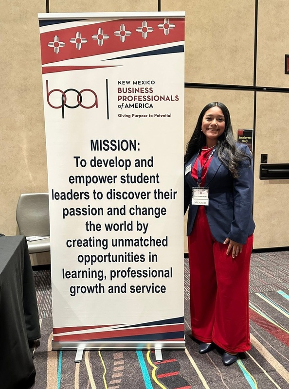 A teen girl in a red pant suit and jacket stands alongside a BPA banner.