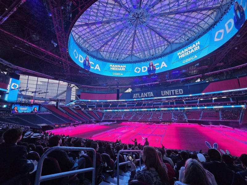 A large arena is pictured, dark and illuminated by blue and pink lights.