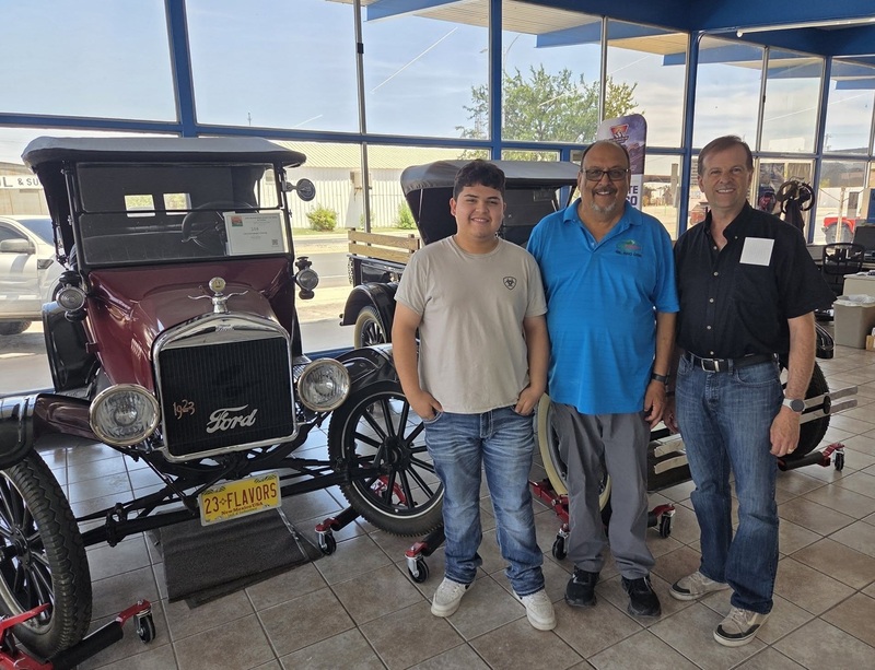 A teen boy stands alongside two men beside a vintage Ford automobile.