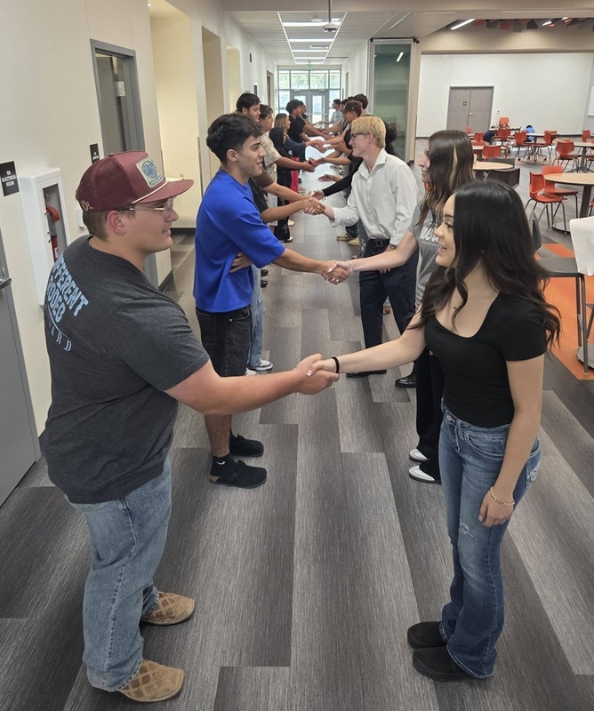 Two long rows of male and female teens stand across from one another and shake hands.