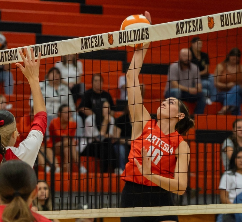 A teen girl in an orange and black volleyball uniform spikes an orange and white ball.