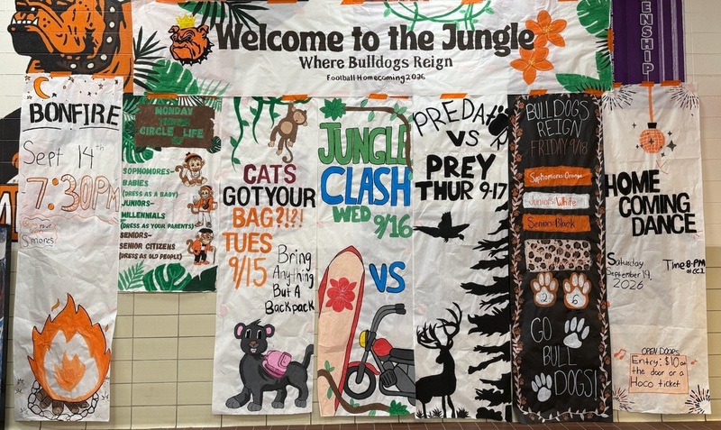 A collection of banners drawn by high-school students hang on a wall. The banners detail information on Homecoming dress-up days.