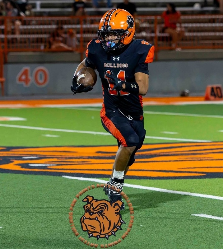 A teen boy in an orange and black football uniform carries the ball in his right elbow as he runs into open field.