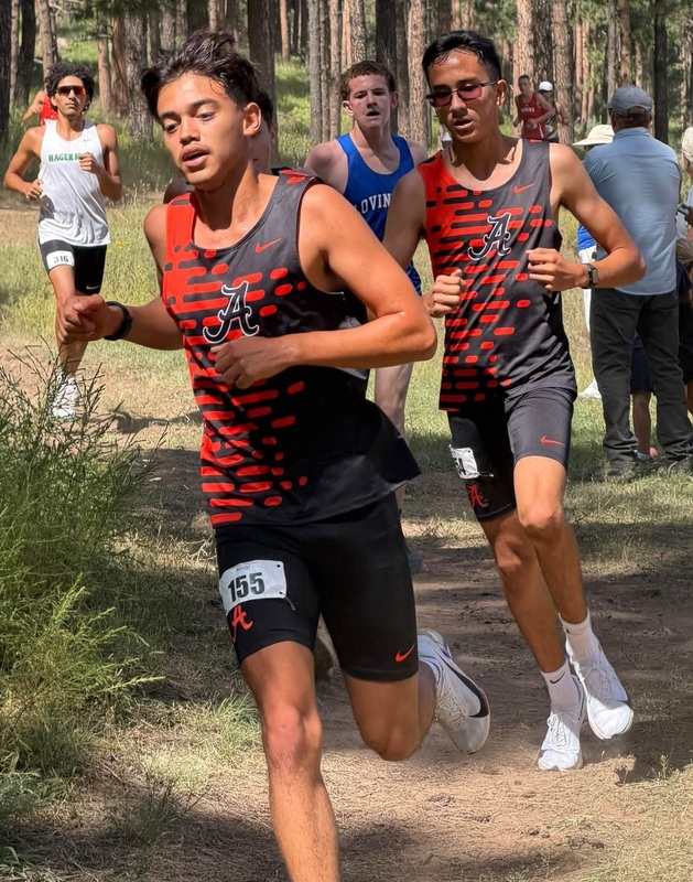 Two teen boys in black and orange cross country uniforms run down a hilly path.