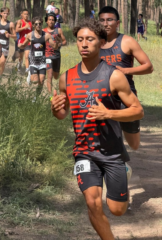 Two teen boys in black and orange cross country uniforms run down a hill with opponents trailing behind.