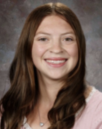 A teen girl with long brown hair and a pink shirt smiles for the camera.