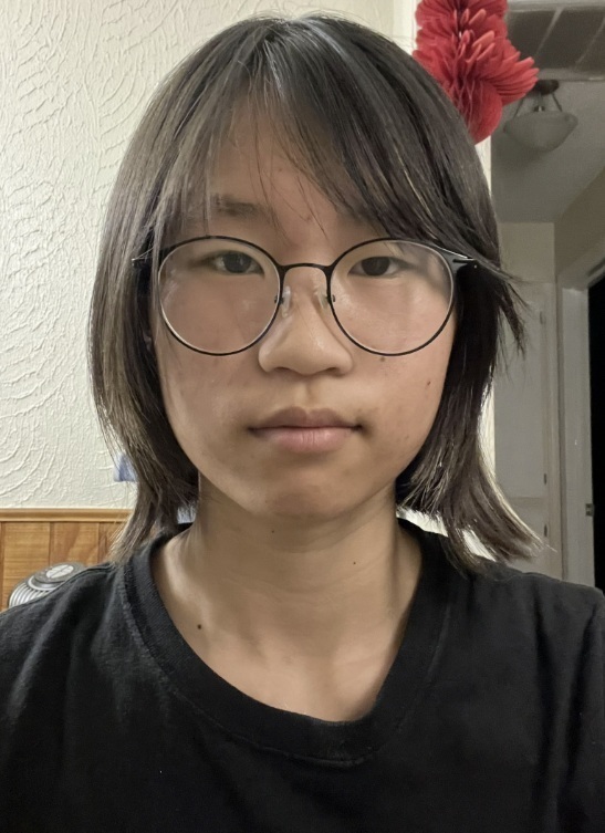 A teen girl with shoulder-length brown hair, large glasses, and a black shirt poses for the camera.
