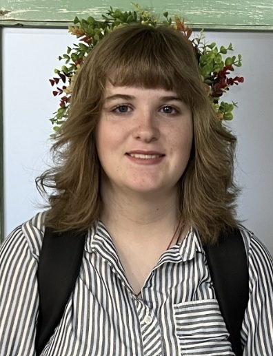 A teen girl with shoulder-length brown hair and a black-and-white striped shirt smiles for the camera.