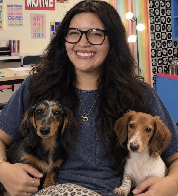 A female with long black hair, glasses, and a navy t-shirt smiles for the camera while holding one small dog in each arm.