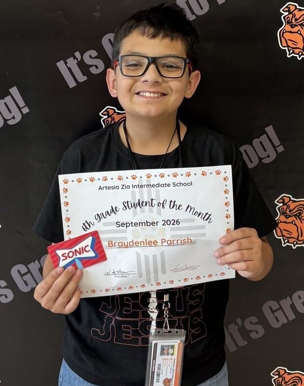 A preteen boy in a black t-shirt and glasses holds a certificate and a Sonic gift card as he smiles for the camera.
