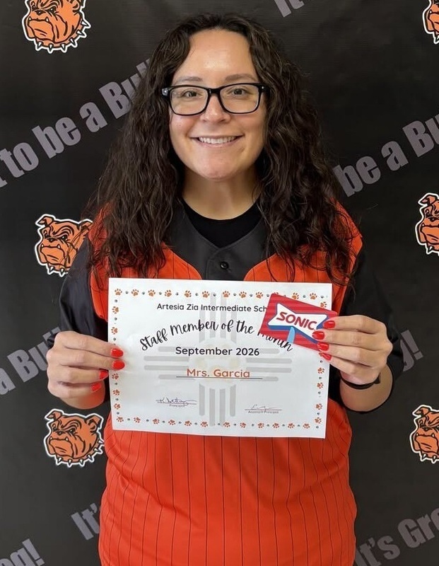 A woman with shoulder-length brown hair, glasses, and a red vest holds a certificate and a Sonic gift card as she smiles for the camera.