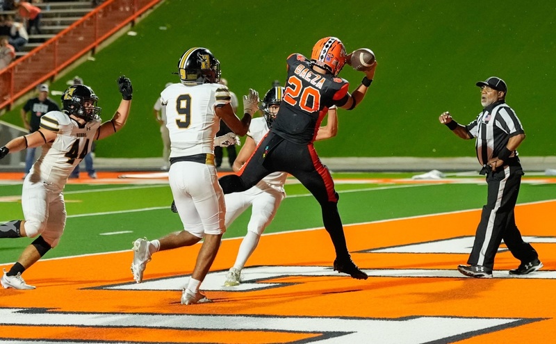 A teen boy in a black-and-orange football uniform catches the football in mid-air in an orange end zone.