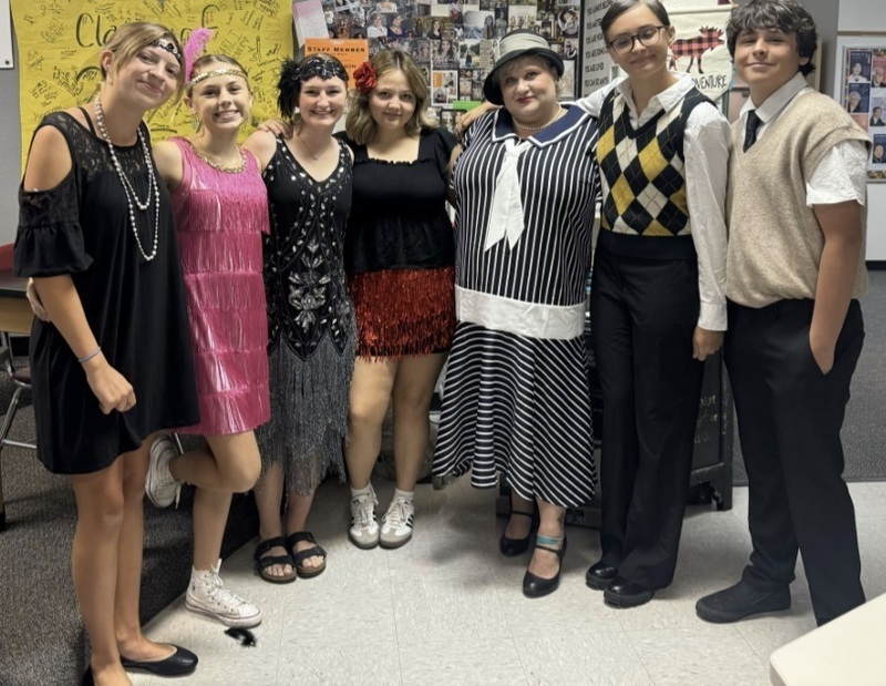 A group of teens poses for a picture while wearing clothes reminiscent of the 1920s.