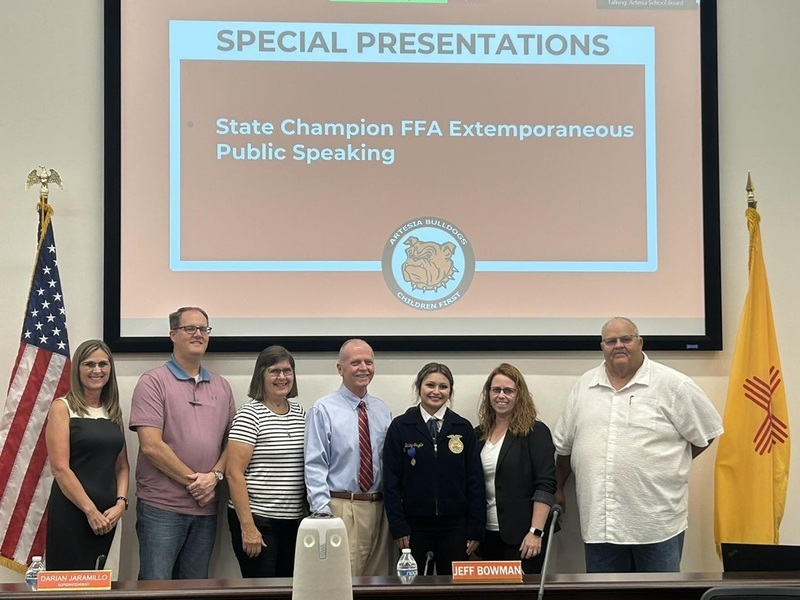 A teen girl in a blue FFA jacket stands beside men and women representing the Artesia school board.