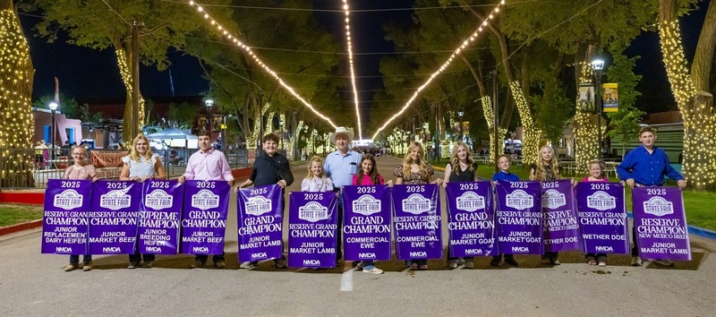 A group of male and female teens stands in a row holding purple Grand Champion and Reserve Champion banners in front of them.