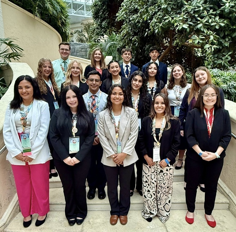 A large group of male and female teens poses for a photo on a staircase in front of trees.