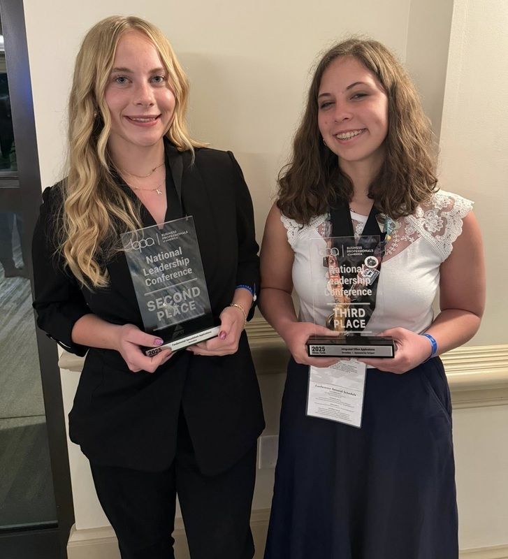 Two teen girls smile for the camera as they hold clear plaques.