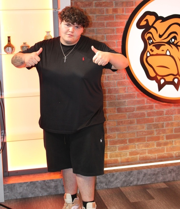 A teen boy in a black shirt and black shorts gives two thumbs up while posting for a photo.