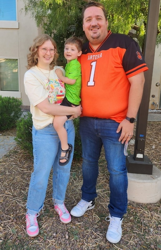 A man in an orange-and-black football jersey stands next to a woman holding a small boy.