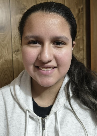 A teen girl in a light-grey hoodie smiles for the camera.