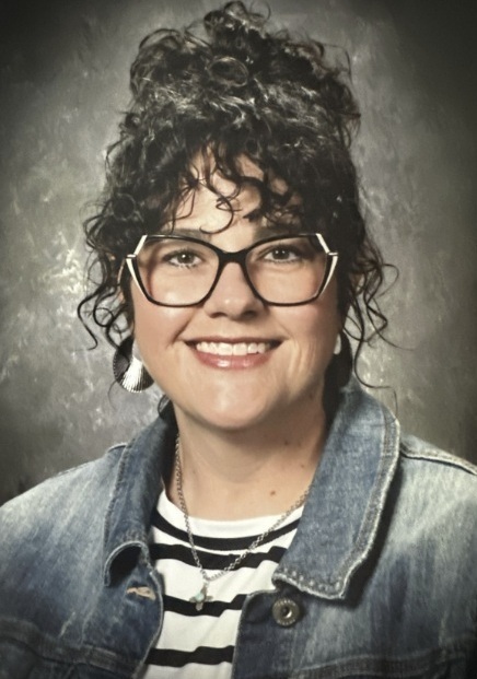 A woman in a black-and-white-striped t-shirt and denim jacket smiles for the camera.