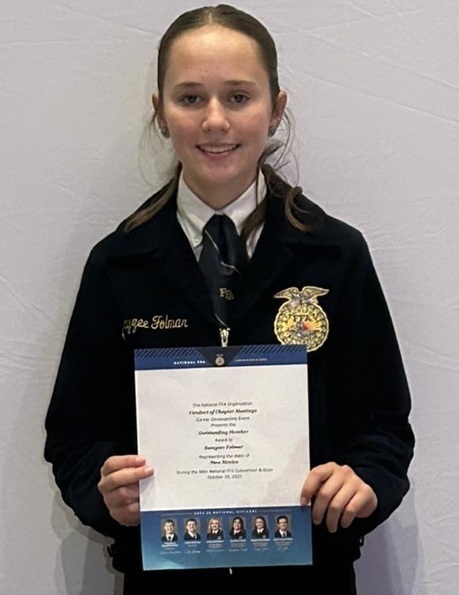 A female teen in an FFA jacket holds a certificate.