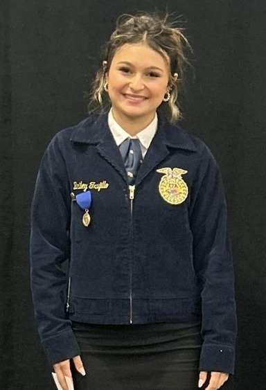 A female teen in an FFA jacket smiles for the camera.