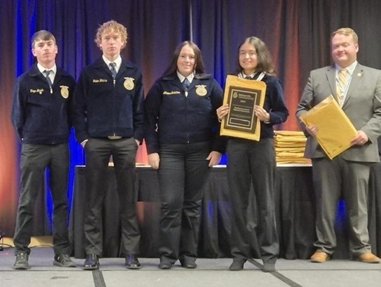 Two male and two female teens in FFA jackets stand alongside an FFA representative in a grey suit. One teen holds a plaque.
