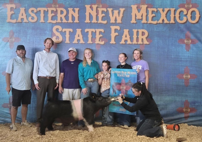 A teen holds a banner behind a pink-and-black pig, surrounded by family members and friends.