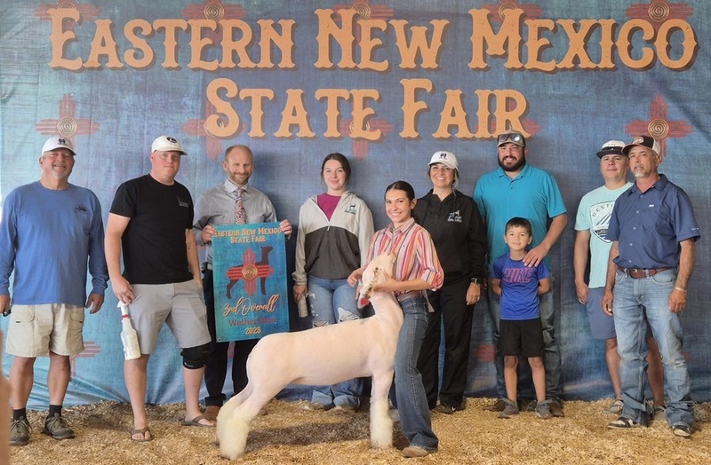A teen girl stands with a white lamb, surrounded by family and friends.