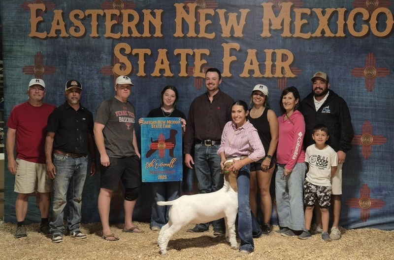 A teen girl stands with a white-and-tan goat, surrounded by family and friends.