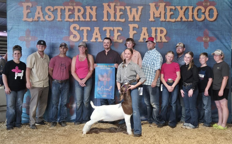 A teen girl stands with a white-and-brown goat, surrounded by family and friends.
