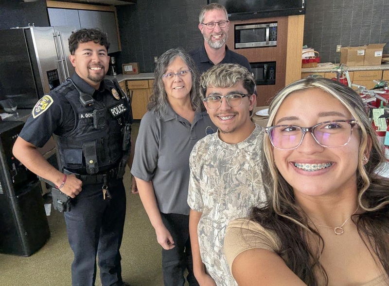 A male and female teen smile for the camera as they stand in front of one female and two male first responders.