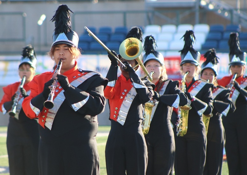 Male and female teens in orange, white and black band uniforms play clarinets, trombones and saxophones.