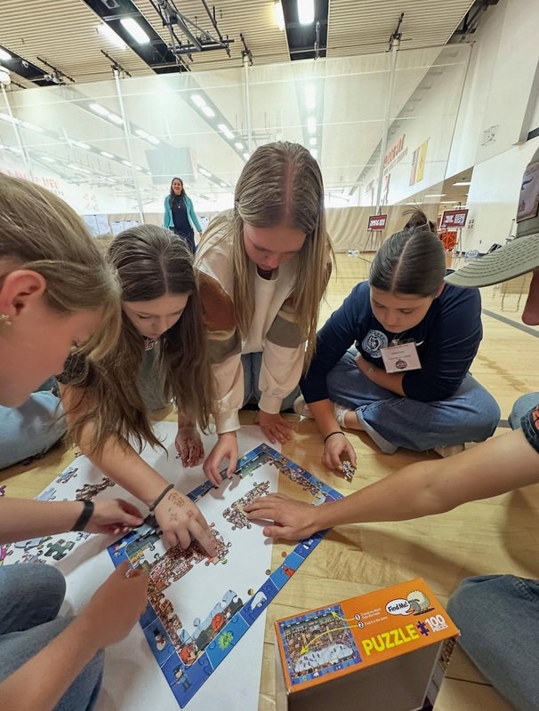 Four female teens are bent over a puzzle assembling pieces.
