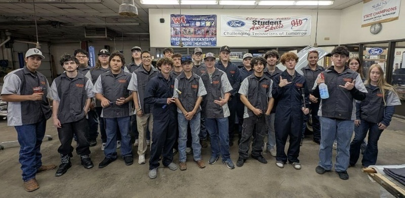 A large group of male and female teens poses for the camera wearing grey work uniforms.