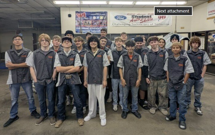 A large group of male teens poses for the camera wearing grey work uniforms.