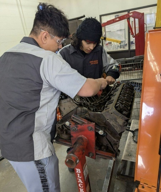 Two male teens bend over an engine.