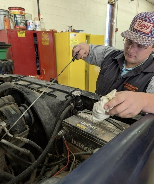 A male teen uses a dipstick to check the oil in a vehicle.