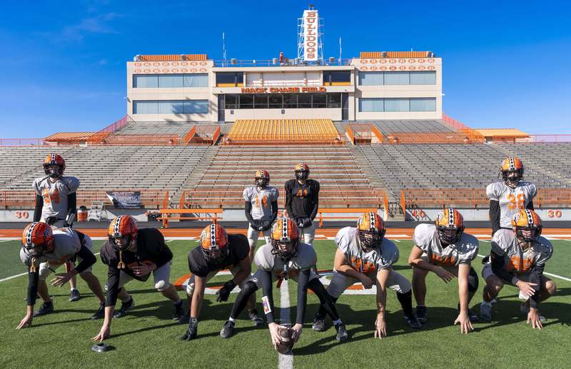A group of boys in practice football uniforms poses in a field goal formation on a football field.