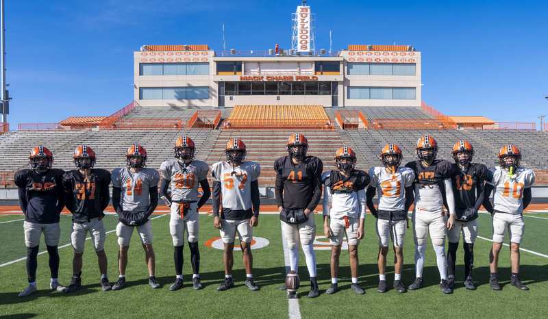 A group of boys in practice football jerseys poses for a photo on a football field.
