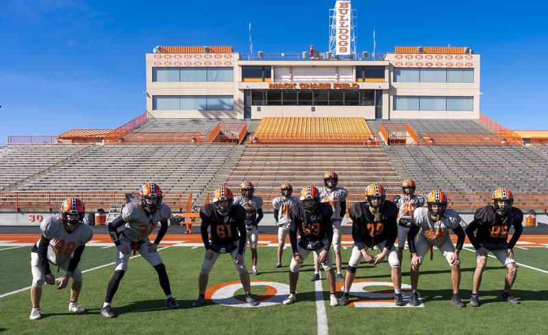 A group of boys in practice football jerseys poses in a kick return formation on a football field.
