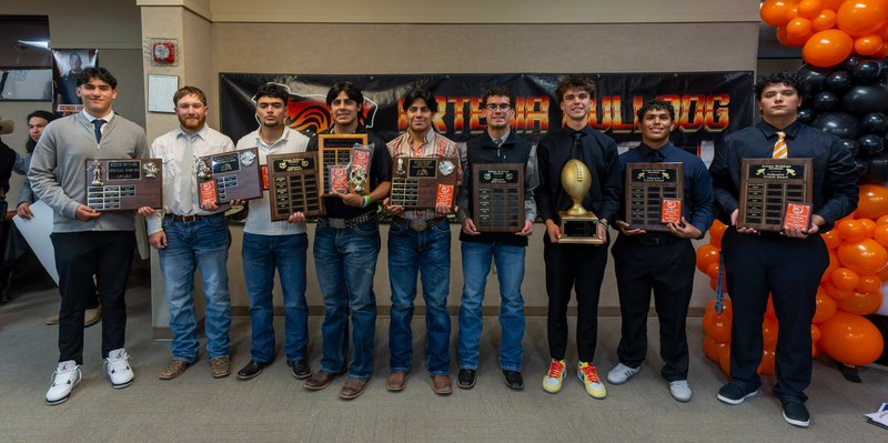 A group of teen boys in dress shirts and pants line up for a picture holding plaques.