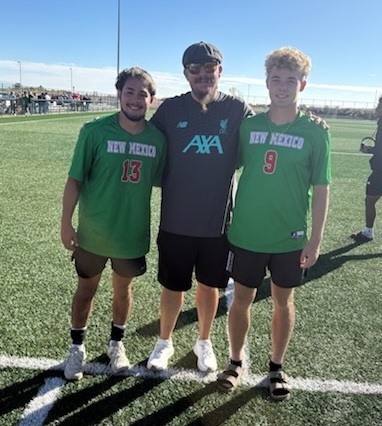 Two teen boys in green soccer jerseys pose for a photo with a male coach.