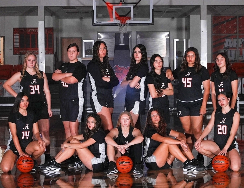 A group of teen girls in black and white basketball uniforms poses for a photo.