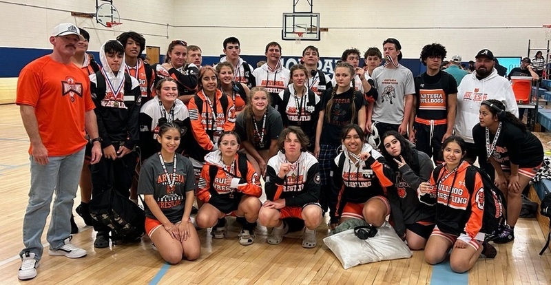 A large group of male and female teens pose for a photo with two male coaches. Some of the teens wear medals.